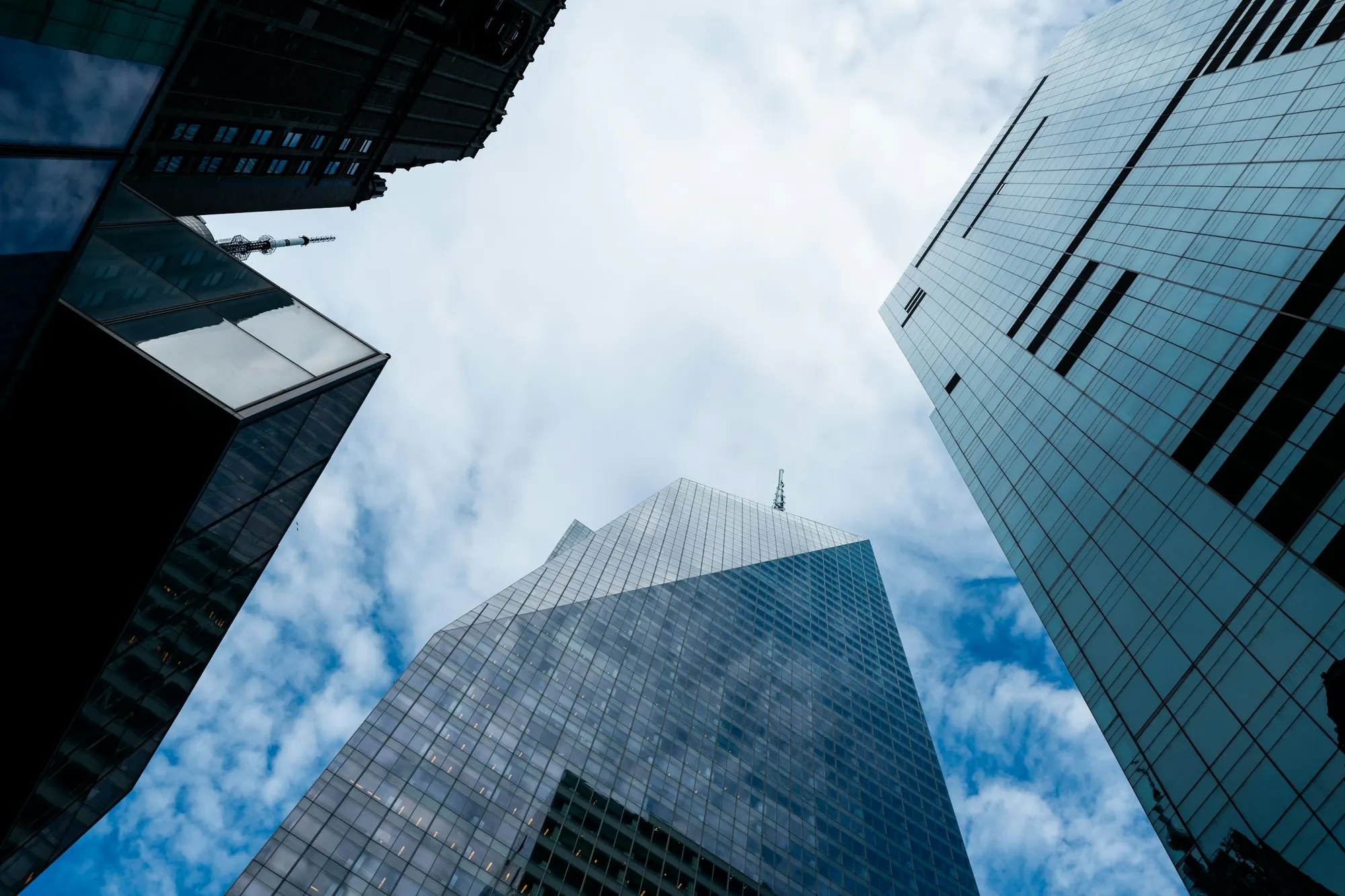 Looking up between glass office towers into a cloudy sky