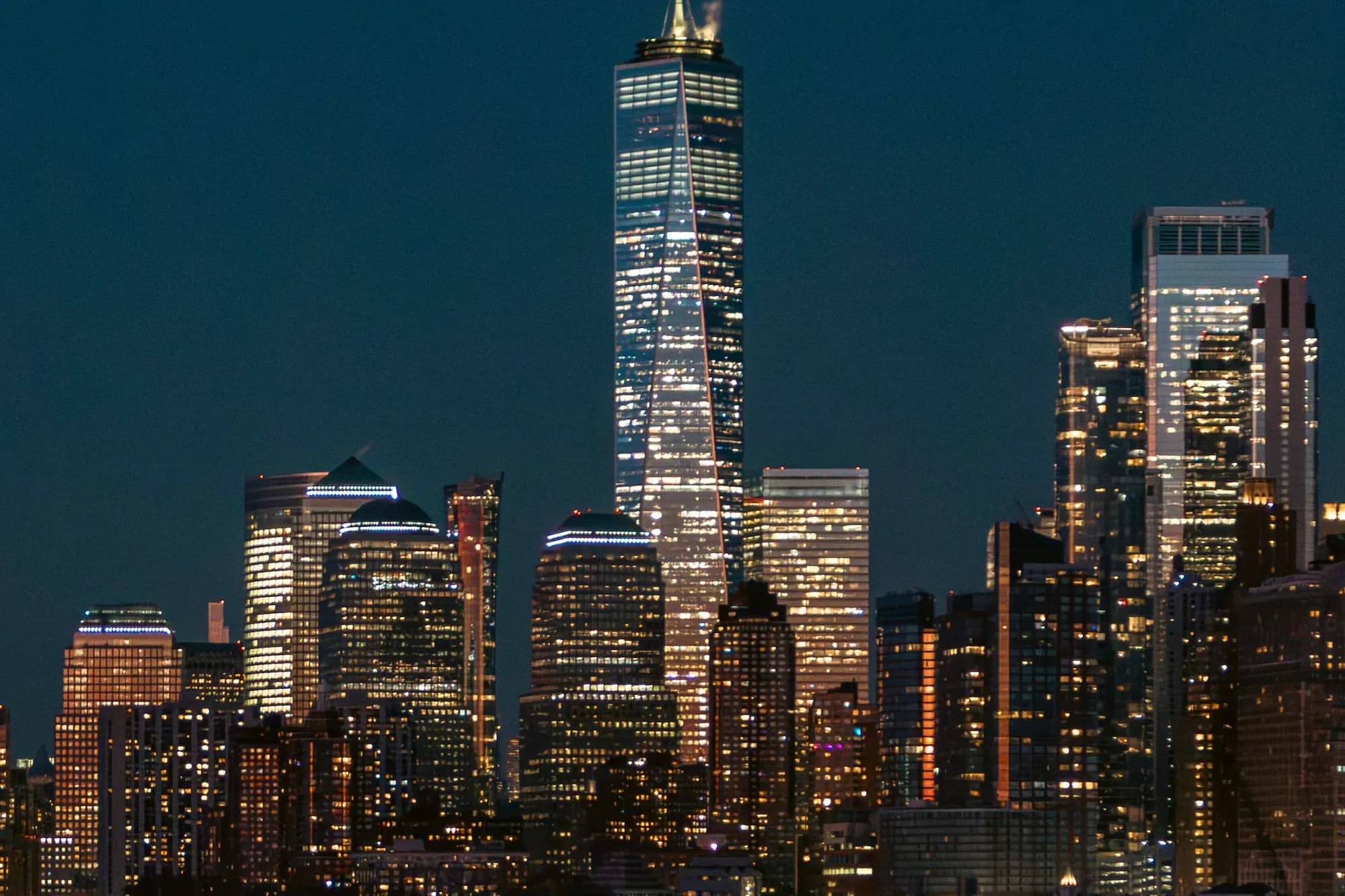 Lower Manhattan’s illuminated office towers at night, led by One World Trade Center